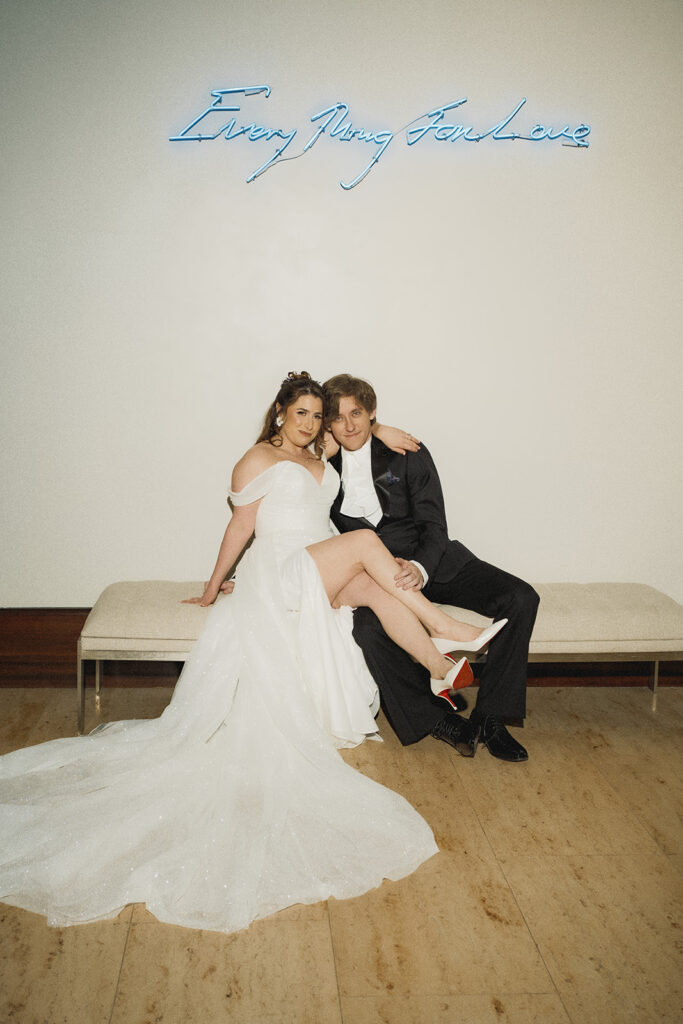 bride and groom pose on a bench together under a neon sign at the alfond inn