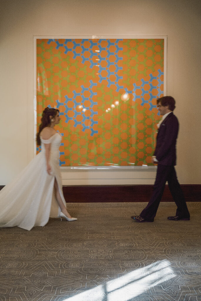 bride and groom walk towards each other in front of a large piece of geometric colorful art on the wall