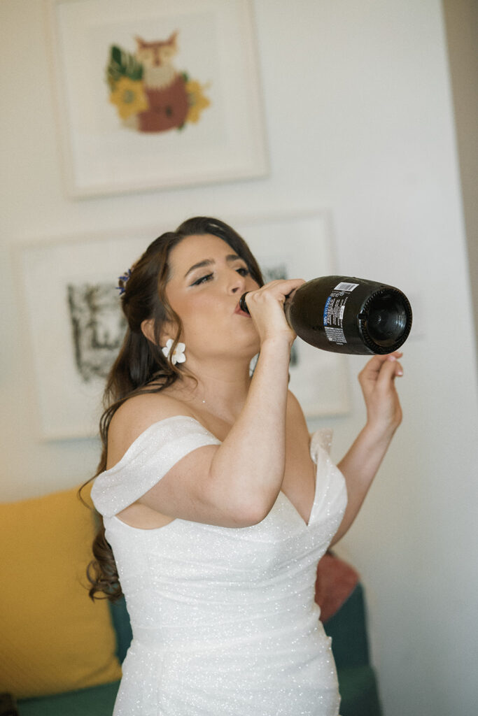 bride takes a drink of champagne from the bottle