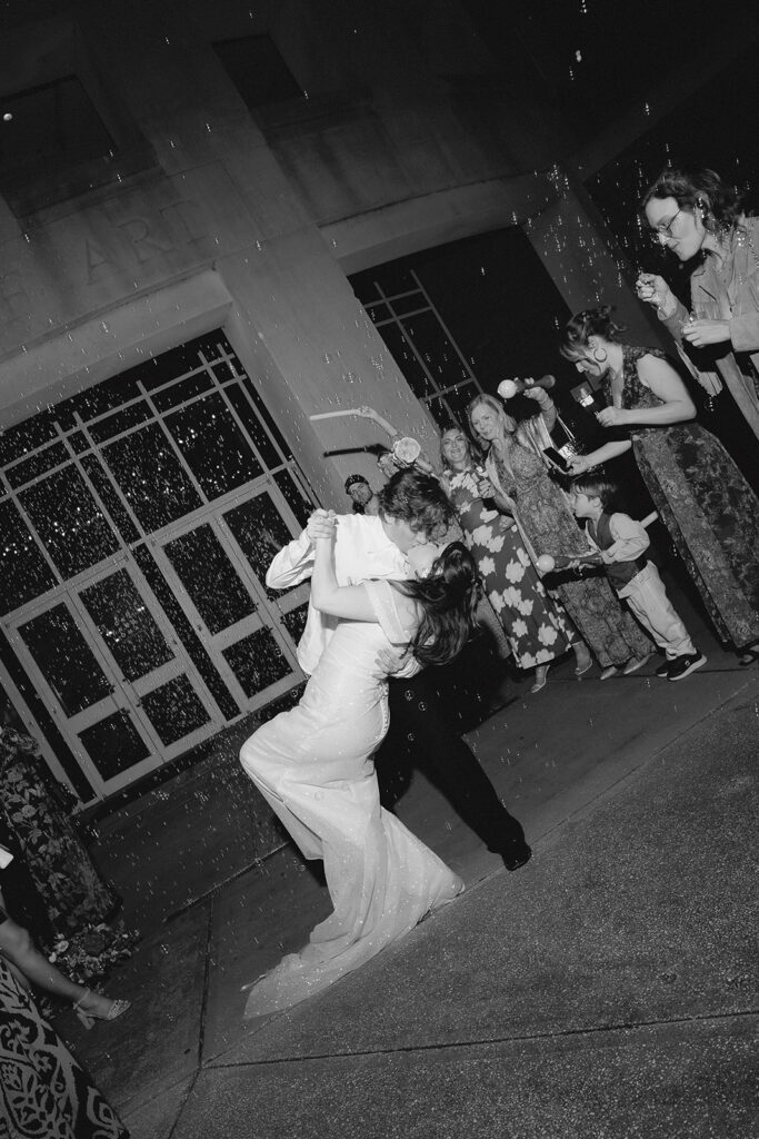 bride and groom dip and kiss at the end of their wedding reception as guests line up outside with bubbles blowing