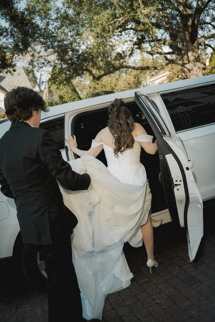 groom carries bride's train as she steps into a limo